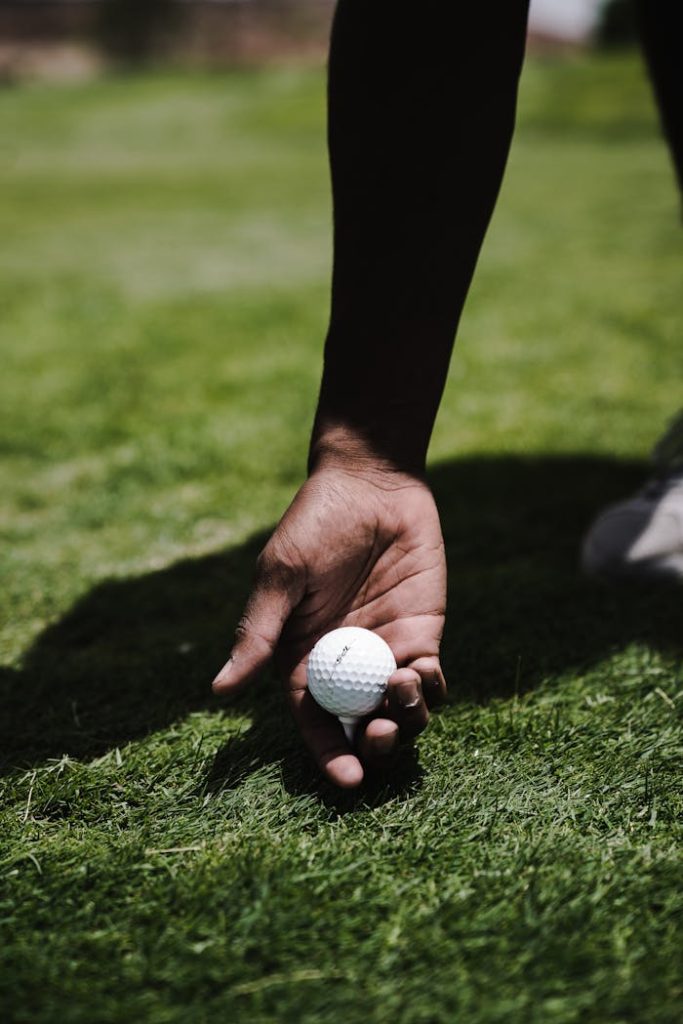 pexels-photo-1325750 A close-up shot of a hand holding a golf ball on a green golf course.