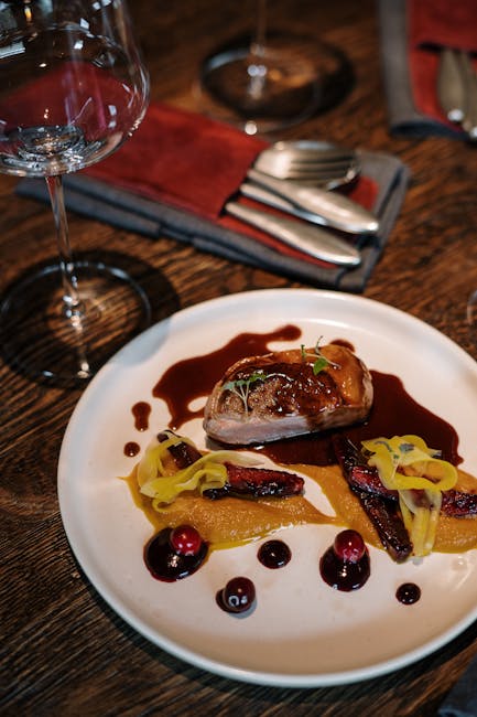 Close-up of a gourmet steak dish elegantly plated with wine glasses in a restaurant setting.